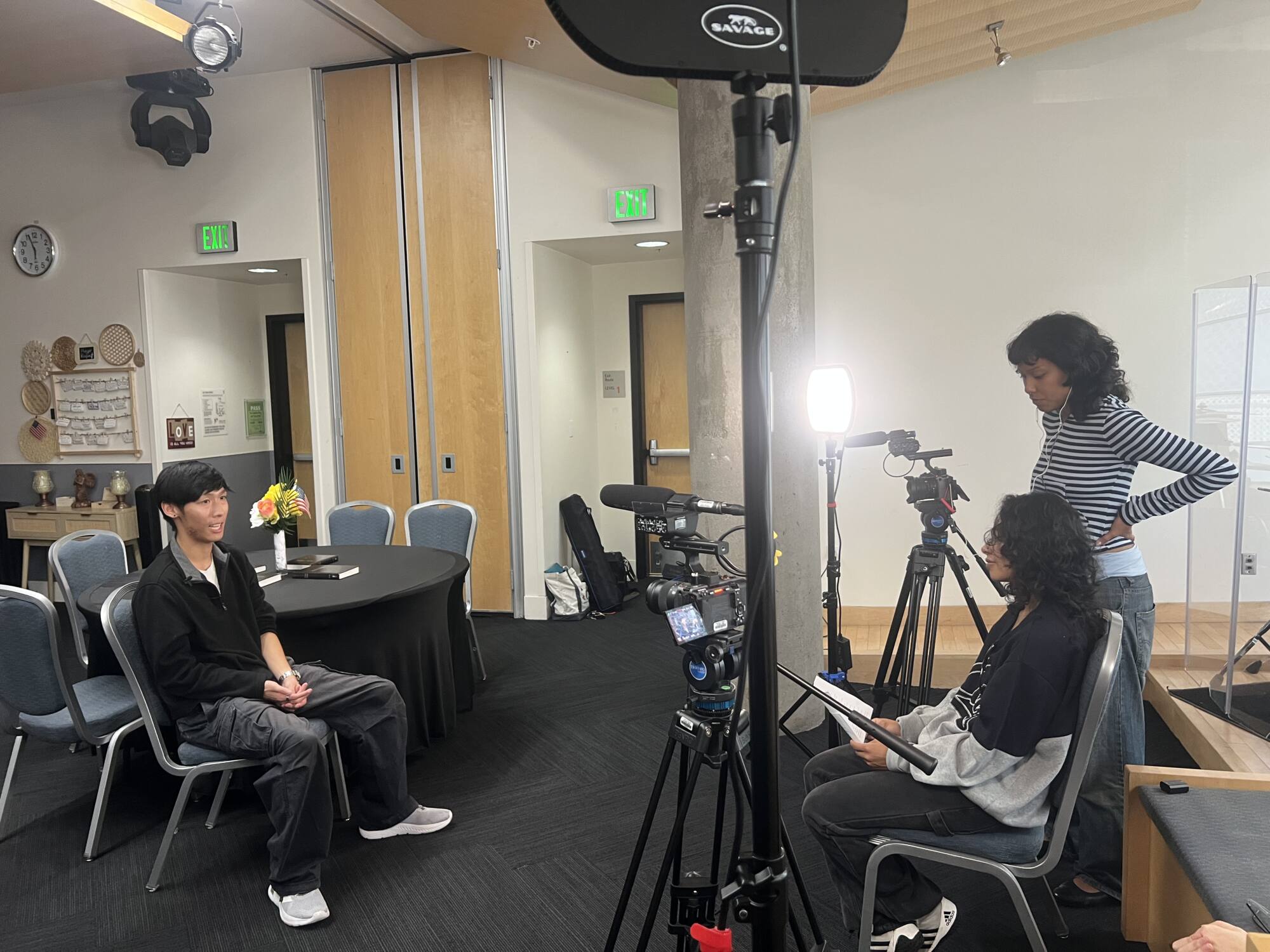 Hire an Apprentice A person with brown hair and wearing a face mask operates a camera.